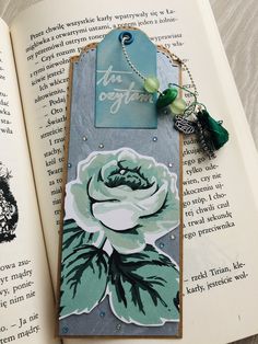 an open book with a tag on it sitting next to a necklace that has a rose on it