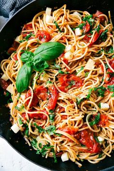 a skillet filled with pasta, tomatoes and parsley on top of a table