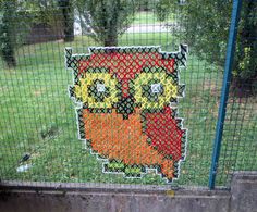 an owl made out of crochet is on the fence in front of a grassy area