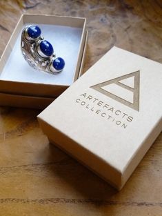 an open box with two rings in it on top of a wooden table next to a pair of earrings