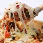 a spoon full of food that is being lifted from the casserole dish with meat and vegetables