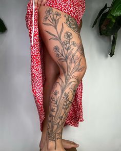 a woman's legs with tattoos and flowers on them, standing in front of a plant