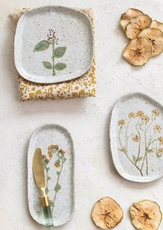 three plates with dried flowers on them next to some slices of fruit and a gold spoon