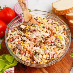 a salad in a glass bowl with a wooden spoon and sliced bread on the side