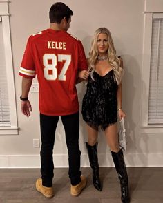 a man standing next to a woman in a black dress and cowboy boots, wearing a football jersey