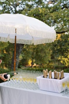 a woman sitting at a table with an umbrella over her head and champagne glasses on the table