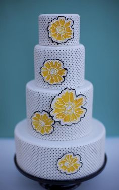 a three tiered cake with yellow flowers on the top and white polka dots around it