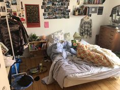 an unmade bed in a cluttered room with lots of pictures on the wall