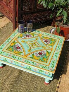 a coffee table painted in bright colors with flowers and leaves on the top, sitting next to a potted plant