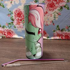 a pink and green cup sitting on top of a table next to a knitting needle