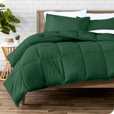 a bed with green comforter and pillows on it in a room next to a brick wall