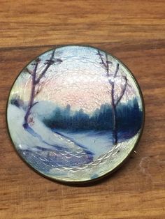 a wooden table with a white and blue plate on it's surface, featuring trees in the snow