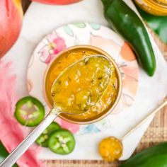 a spoon full of sauce sitting on top of a plate next to peppers and an apple