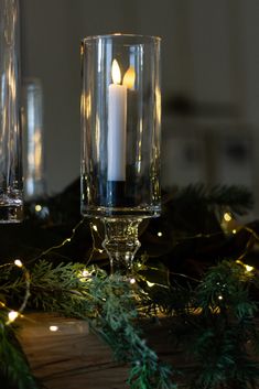 a lit candle sitting on top of a wooden table next to two glasses filled with water