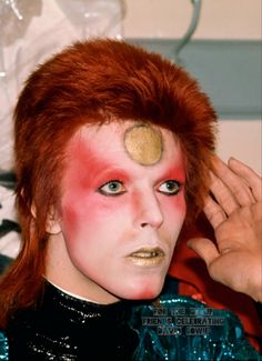 a man with red hair and makeup has his face painted gold