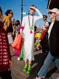 a woman in white dress and green shoes walking down the street with other people behind her