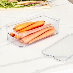 some carrots are sitting in a plastic container on a counter next to a cutting board