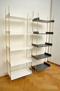 three black and white shelving units in a room with wood floors, one is leaning against the wall