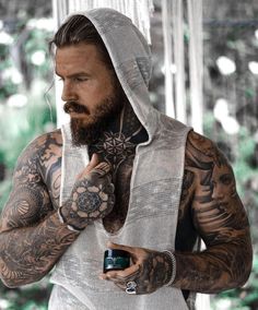 a man with tattoos and a hoodie holding a cell phone