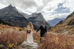 a bride and groom holding hands in the mountains