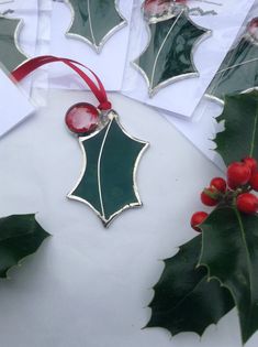 some christmas decorations are laying out on a white surface with red ribbon and holly leaves