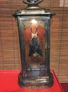 an old fashioned lantern with a bat hanging from it's side on top of a red table