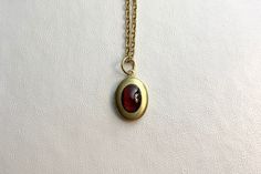 "This sweet, small, OVAL antique brass locket has a smooth Natural Garnet cabochon set on the front.  It hangs on a 16\" gold stainless steel chain necklace.  The locket is approximately 11x16mm.  The cabochon is 6x8mm.  Arrives in an eco-friendly jewelry box, ready for gifting. MORE lockets in my shop! FREE SHIPPING! THANK YOU FOR VISITING MY SHOP!" Classic Brass Jewelry With Cabochon, Antique Gold Oval Cabochon Necklace, Antique Gold Necklace With Oval Cabochon, Victorian Gold Necklace With Oval Cabochon, Victorian Gold Oval Cabochon Necklace, Classic Brass Locket Necklace With Vintage Charm, Brass Cabochon Round Pendant Necklace, Brass Cabochon Oval Pendant Jewelry, Bronze Oval Necklaces With Vintage Charm