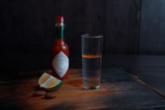 a bottle of hot sauce next to a shot glass and almonds on a wooden table