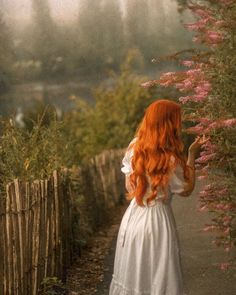 a woman with long red hair walking down a path