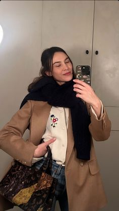 a woman taking a selfie in front of a mirror wearing a coat and scarf