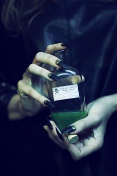 a woman holding a bottle of alcohol in her hands with black and white nail polish