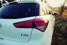 the rear end of a white car parked in a grassy area with trees and bushes