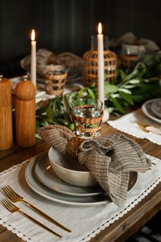 a table set with place settings, candles and napkins on top of the plates