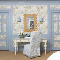 a bedroom with blue walls and floral wallpaper on the walls, a white chair in front of a small desk