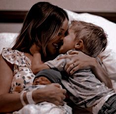 a woman and child are laying on a bed together, one is kissing the other