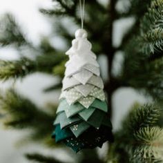 a christmas tree ornament hanging from the top of a pine tree with white and green decorations