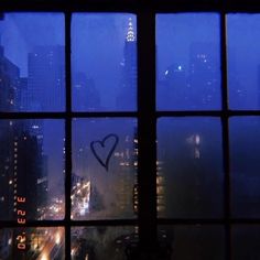 a window with a heart drawn on it in the middle of a city at night