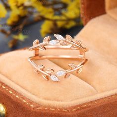 a gold ring with leaves and stones on it sitting in a velvet box next to flowers