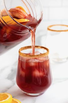 a pitcher filled with liquid pouring into a glass next to sliced lemons and orange slices