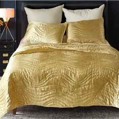 a bed with yellow comforter and pillows in a dark room next to a night stand