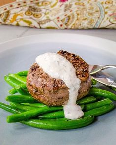 a white plate topped with green beans and meat covered in ranch dressing next to a fork