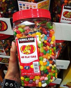 a person holding a jar full of jelly beans in front of candy store display shelves