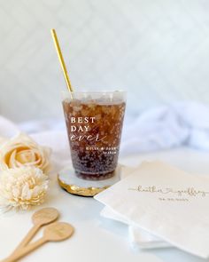 a glass filled with liquid sitting on top of a table next to napkins and flowers