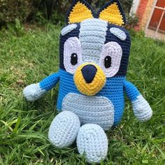 a crocheted blue and yellow stuffed animal sitting in the grass with it's eyes closed