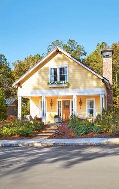 a yellow house with white trim on the front door and two windows, surrounded by trees