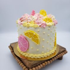 a decorated cake with lemons, oranges and pink icing on a wooden platter