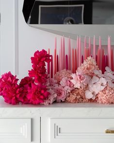 pink candles and flowers sit on a white countertop in front of a mirror that is reflecting the light