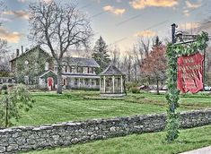 a house with a sign in front of it on the side of a road next to a stone fence