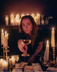 a woman sitting at a table with candles in front of her and cards on the table