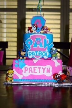 a pink and blue birthday cake with paw patrol characters on the bottom tier is sitting on a table